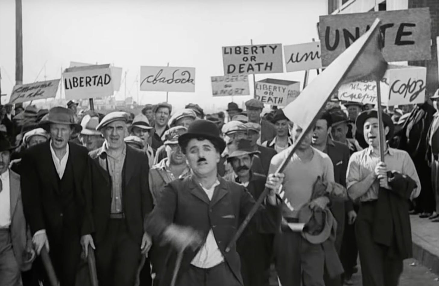 Charlie Chaplin as the tramp leads a workers' protest march in 1936 film Modern Times. He waves a red flag, others carry placards saying 'libertad', 'unity', 'freedom' and other terms