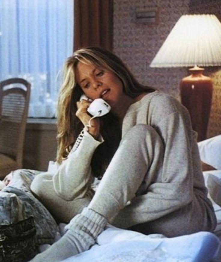 This may contain: a woman sitting on a bed talking on the phone while holding a cup in her hand