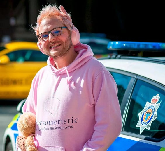 A person wearing pink hoodie and glasses with a teddy bear and police car

Description automatically generated