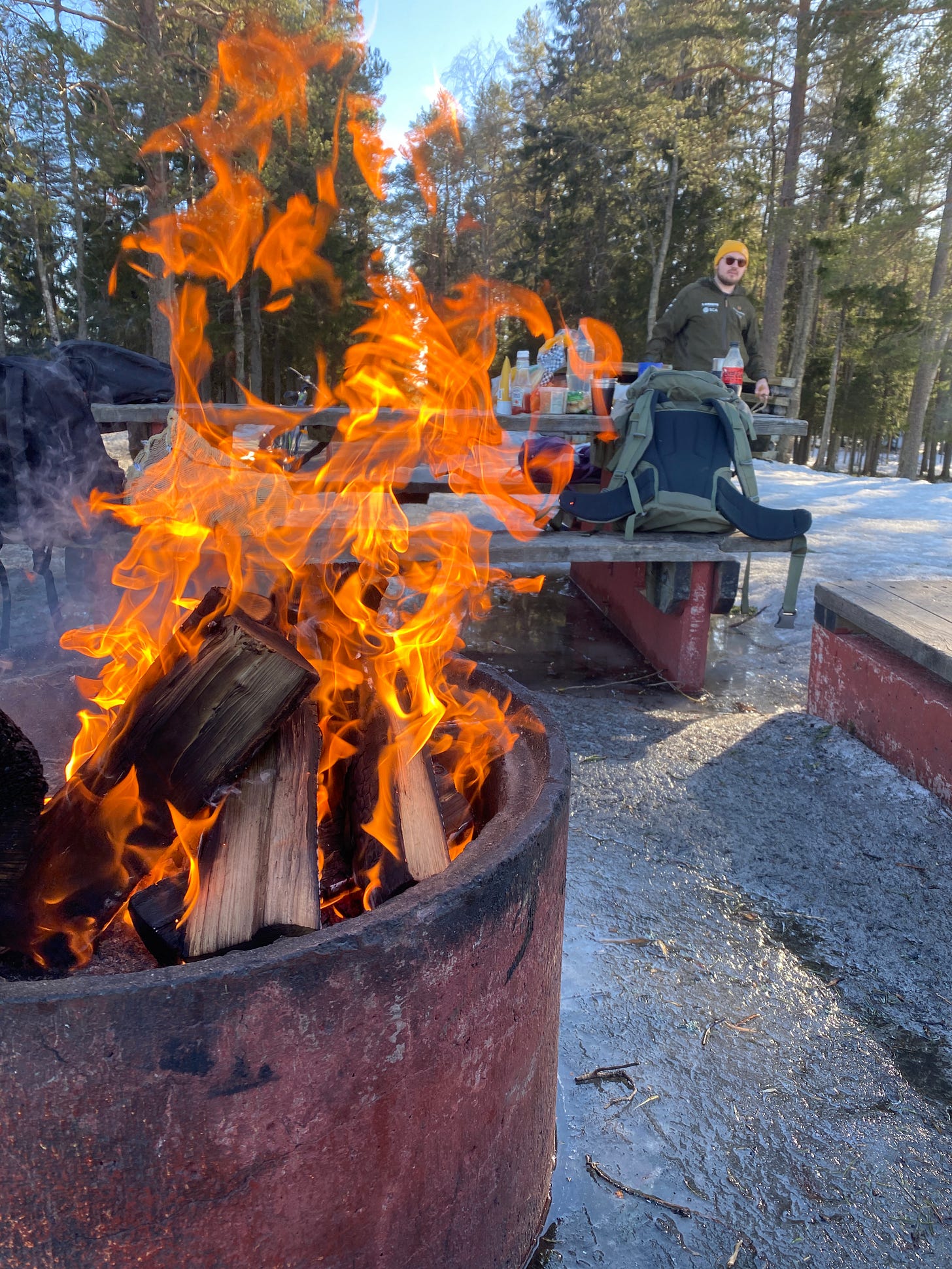 Blazing campfire in a pit surrounded by ice, evergreen trees, and snow