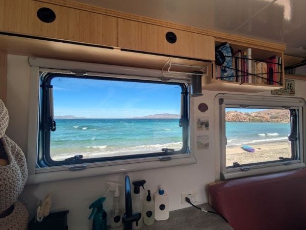 the view from inside our truck looking out through the windows at a sandy beach and the ocean in layers of turquoise and blue with small whitecap waves