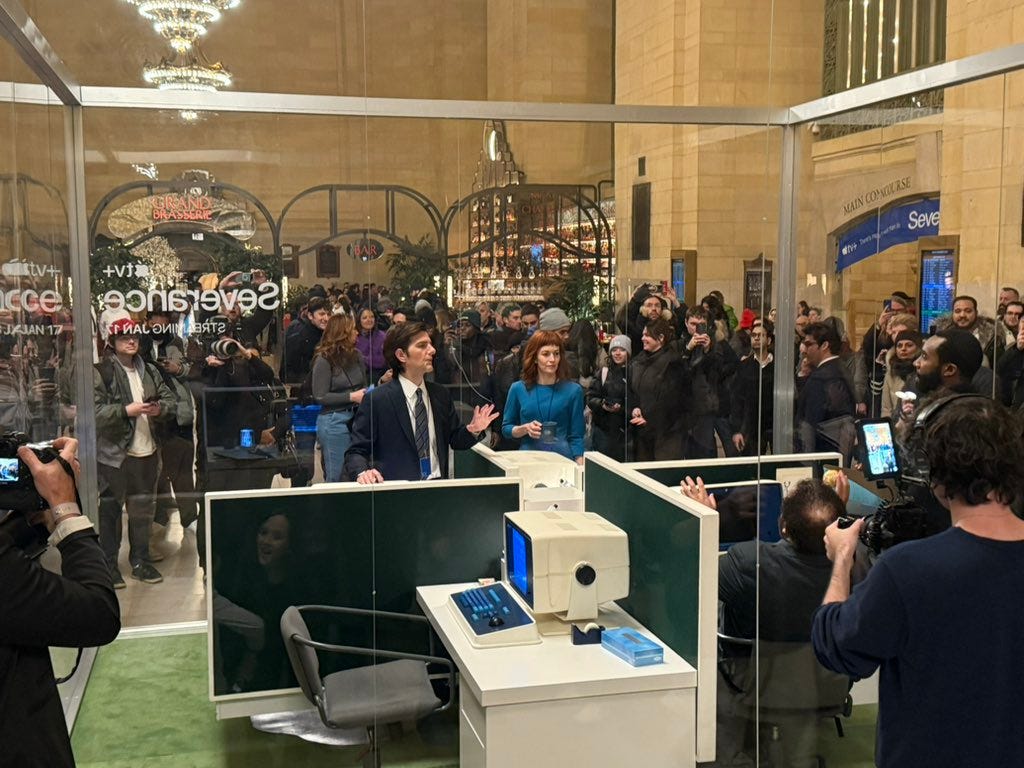 Severance pop-up in Grand Central Station -- actors are inside a glass cube that contains their desks and computers