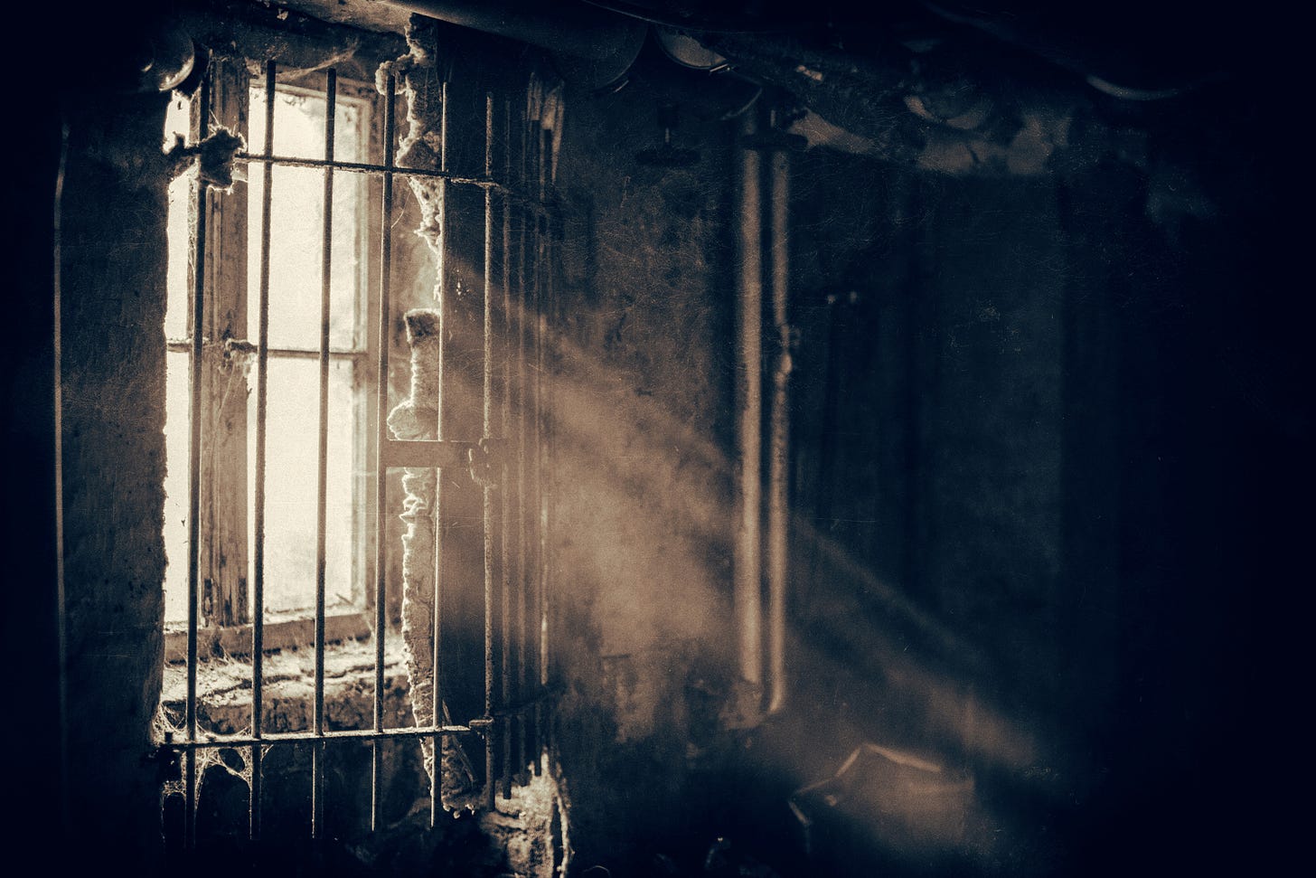 Light shines through a prison window with bars over it. The prison resembles a dungeon.