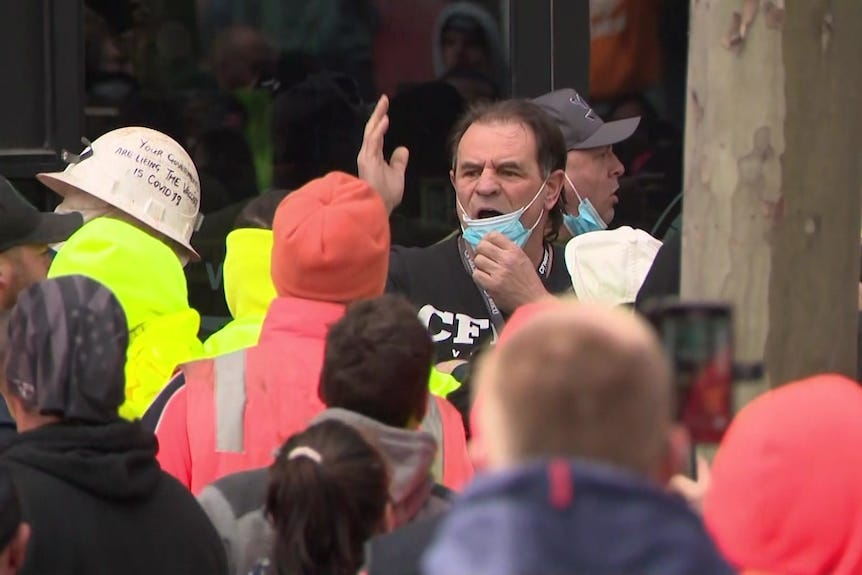 John Setka pulling down a facemask surrounded by people in high-viability vests.