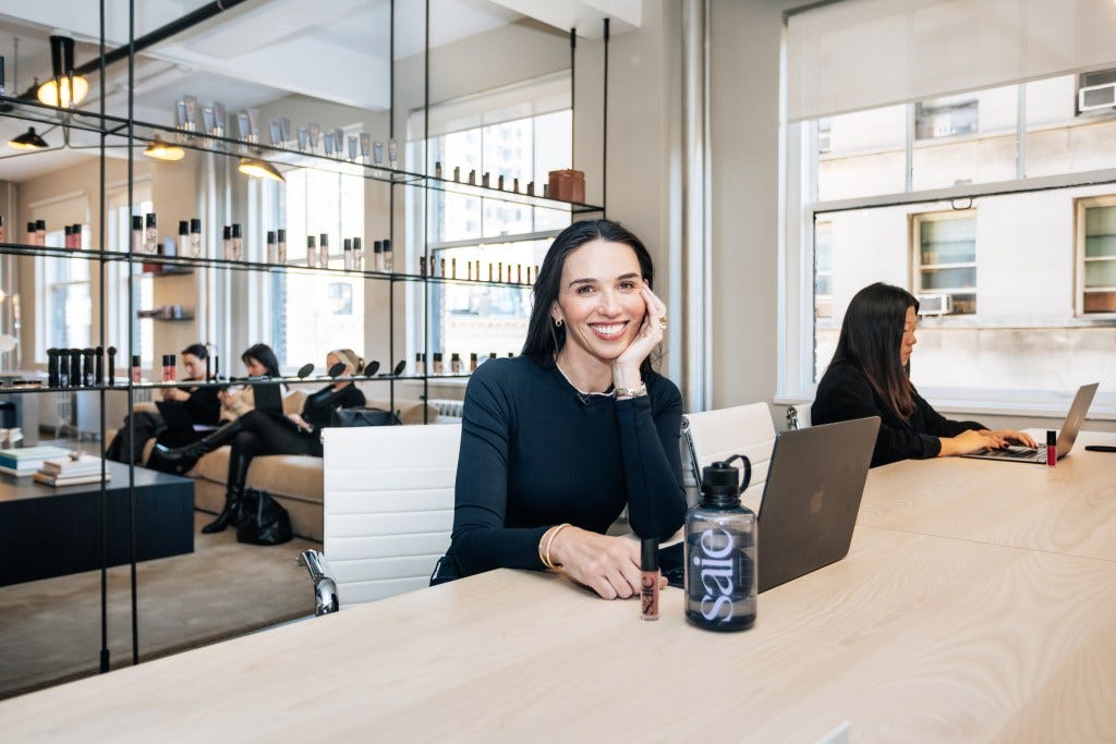 Laney Crowell, founder and CEO of Saie, sitting at a table with a laptop and a bottle in the Saie office in Chinatown, Manhattan.