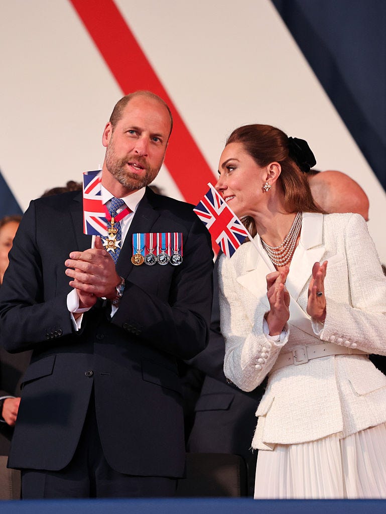 Prince William and Princess Kate holding UK flags and looking out