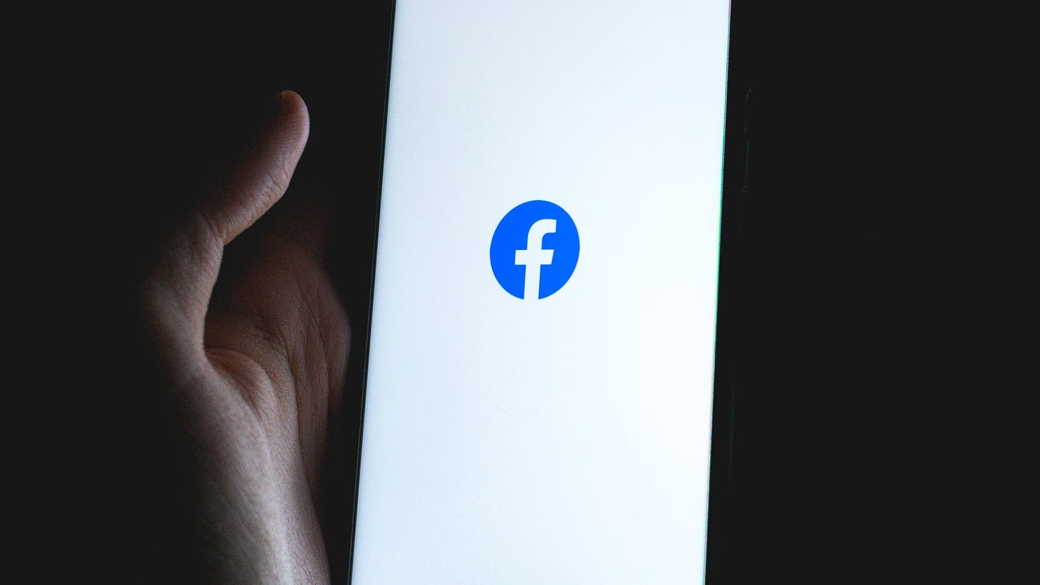 A hand holds a phone with the Facebook logo in a dark area.