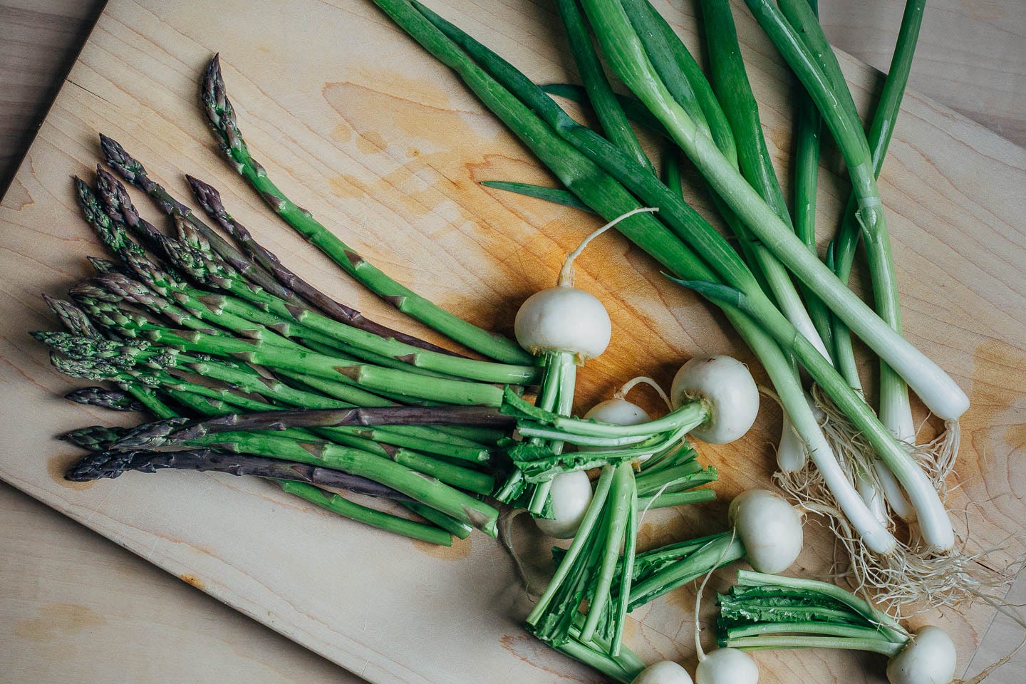 A cutting board with turnips, spring onions, and asparagus