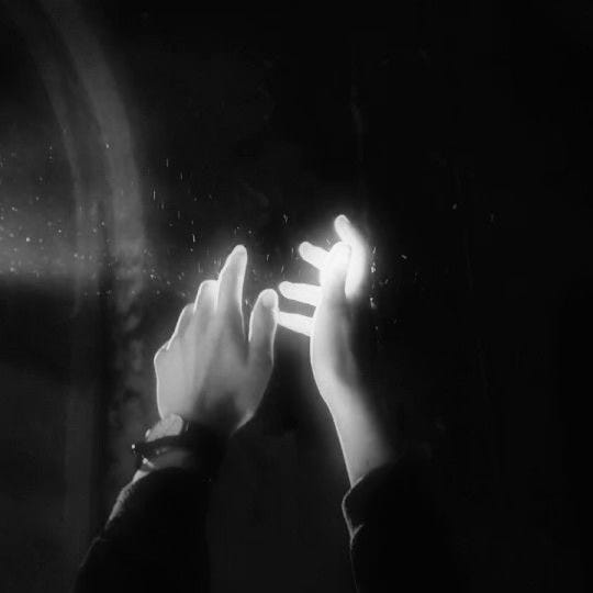 black and white hazy image of hands reaching up to the light