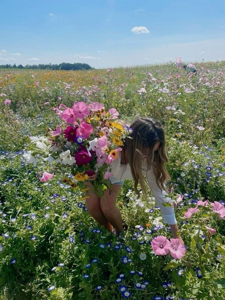 This may contain: a woman kneeling down in a field full of wildflowers and holding a bouquet of flowers