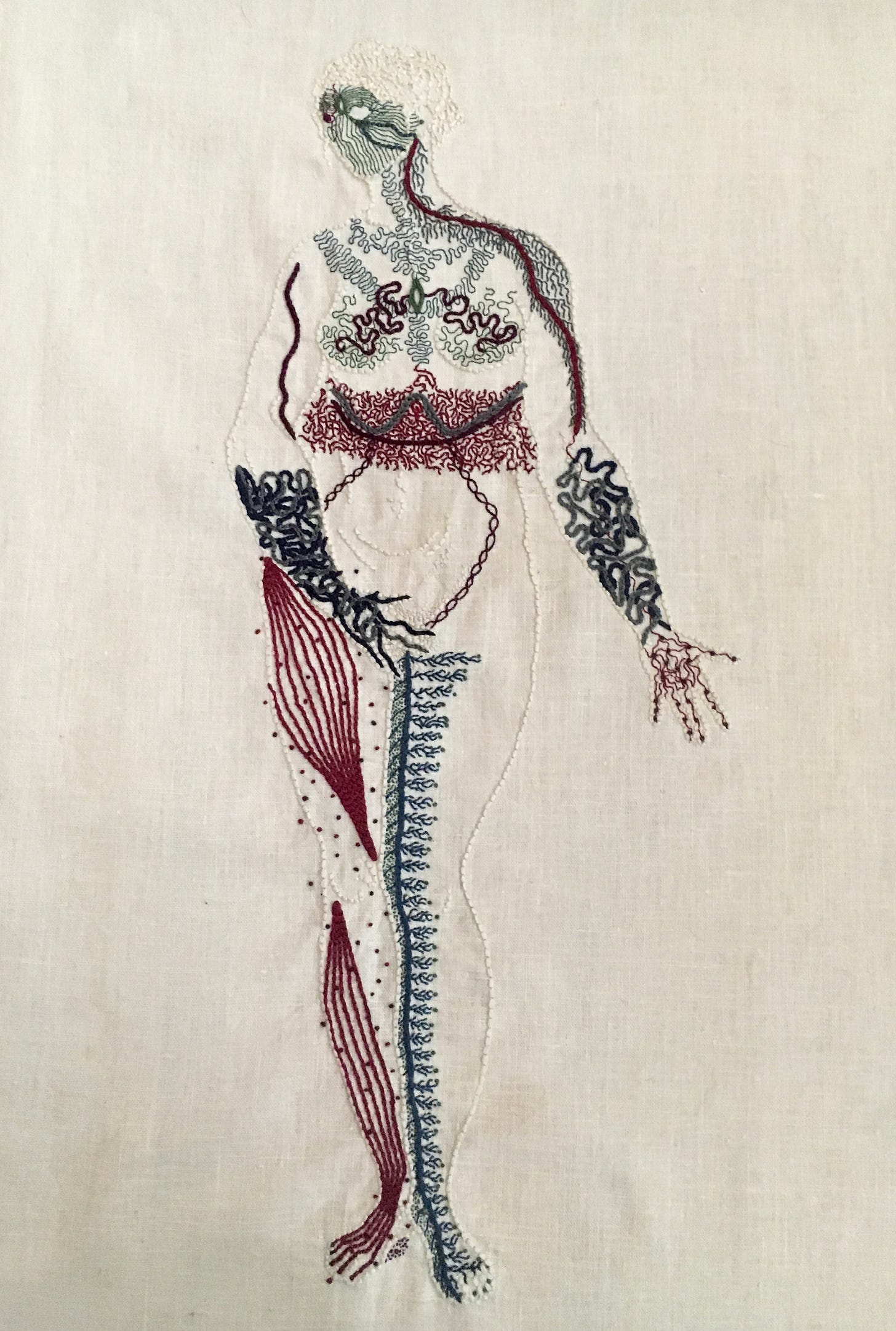 Body Map (2016)  An outline of a naked woman is embroidered on linen in the same bone white colour as the linen. She stands legs together, her right hand covering her groin, her left hand, palm up, extended slightly to her side. She looks to the right. Her entire body except for her belly is covered in intricate markings representing different neurological sensations. Her face is a mask of green lines, feathery grey lines cover her shoulders and chest. There is a thick band of intricate burgundy stitching around her waist. Her forearms and hands are covered in thick blue undulant lines. Her right leg has bands of burgundy along the muscles, with small dots around them. Her inner left leg has a thick line of blue running up it, with thin branches spreading towards her outer leg.