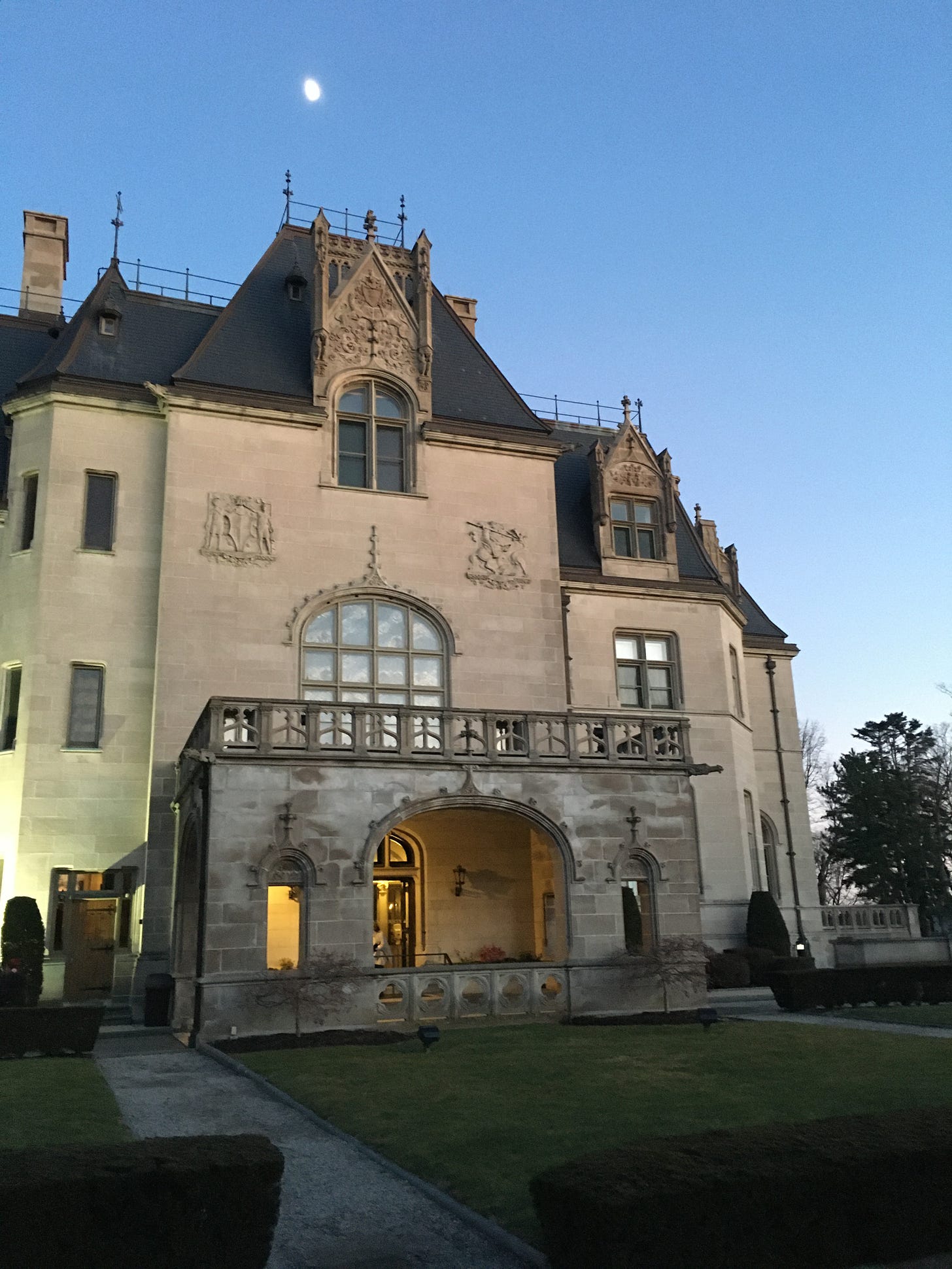 Ochre Court, a mansion made of marble with a slate roof, stands at night against a full moon. 