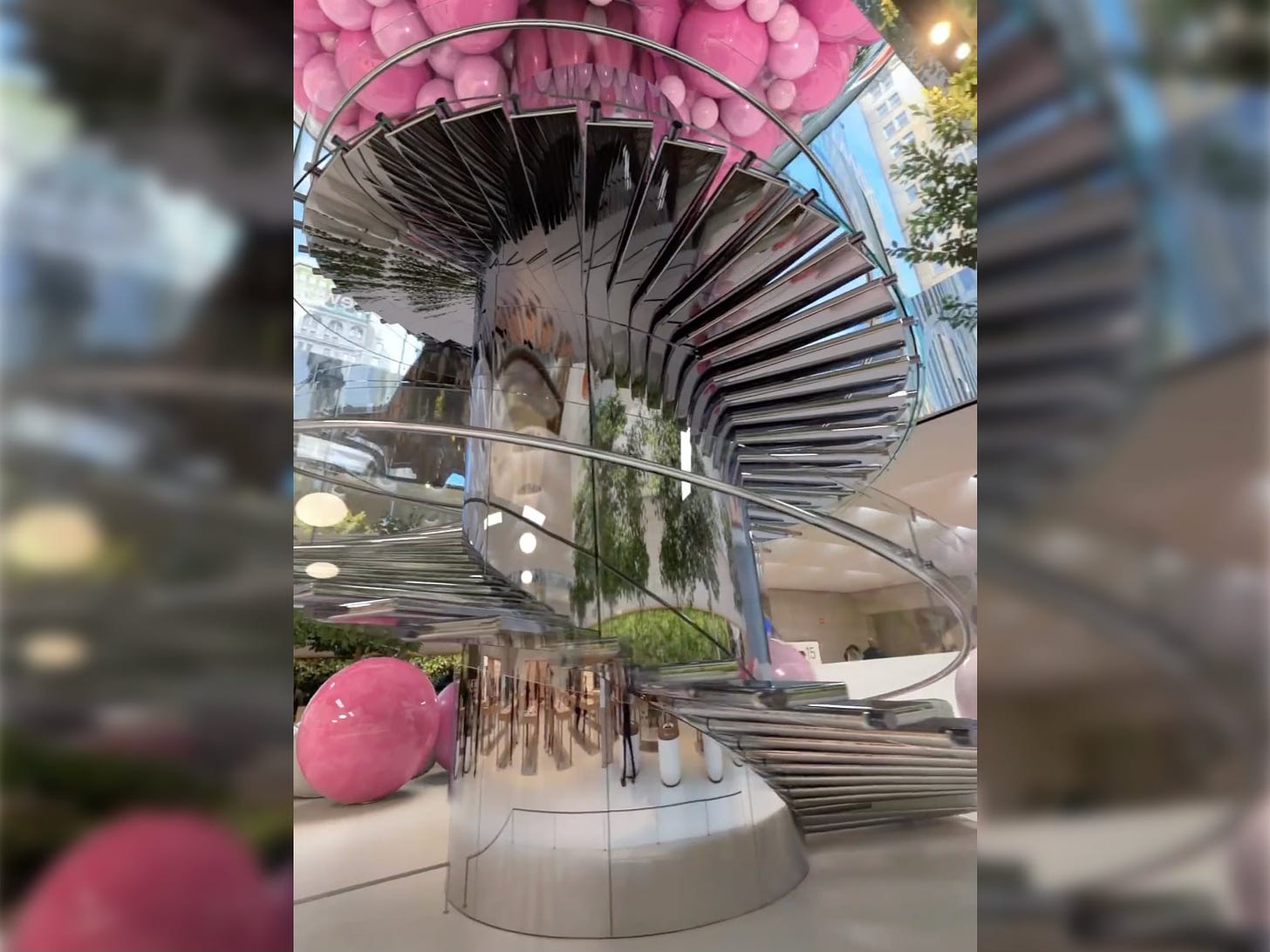 A frame from a CGI clip shot at Apple Fifth Avenue. Pinks bubbles fill the cube and are rolling down the staircase.