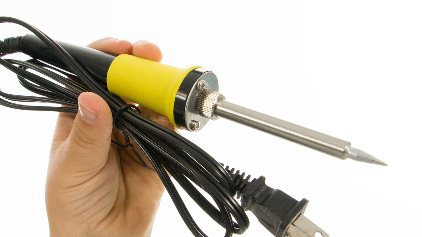 Picture of a soldering iron, with the power cord coiled up, held up by the apparent photographer's left hand.