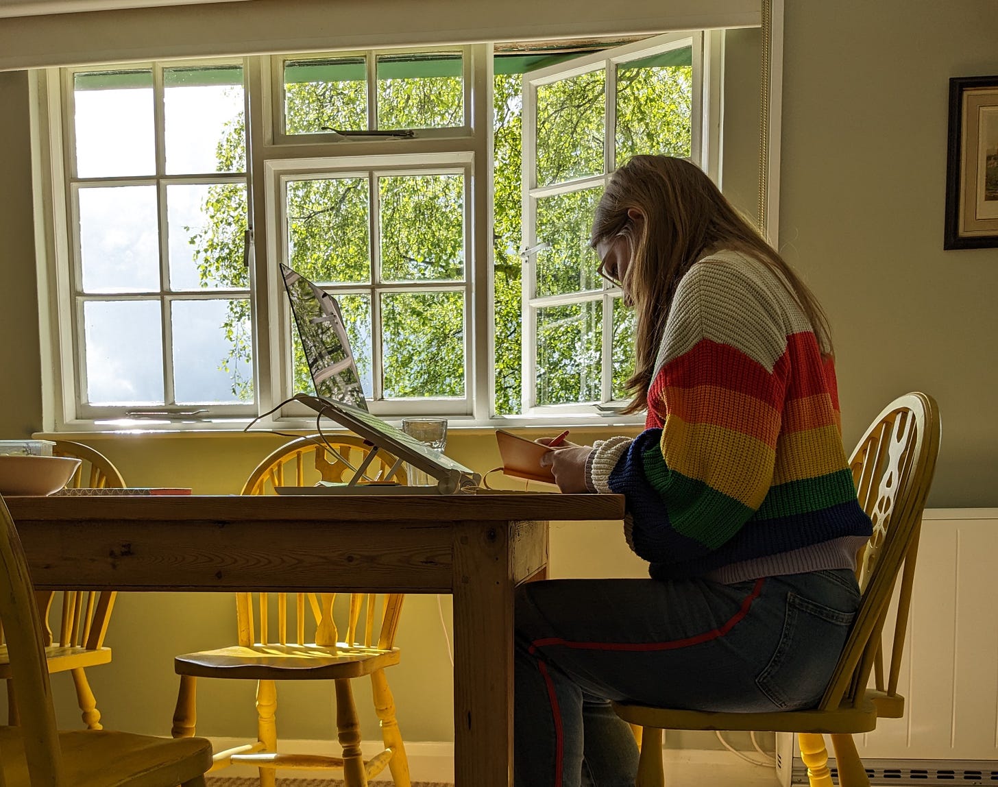 Libby Page sat at a desk writing, with a window behind and a view of trees