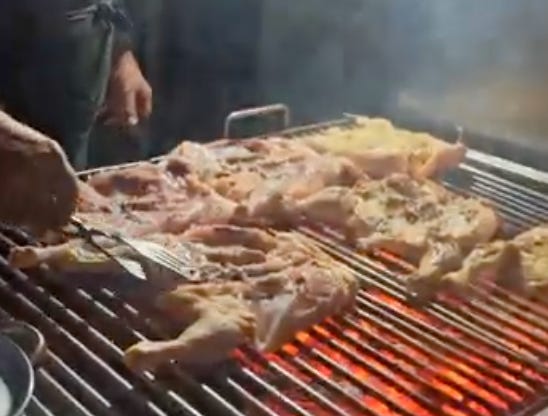The Chicken Guy works the grill at his churrasquiera, rotating chickens over a flame.