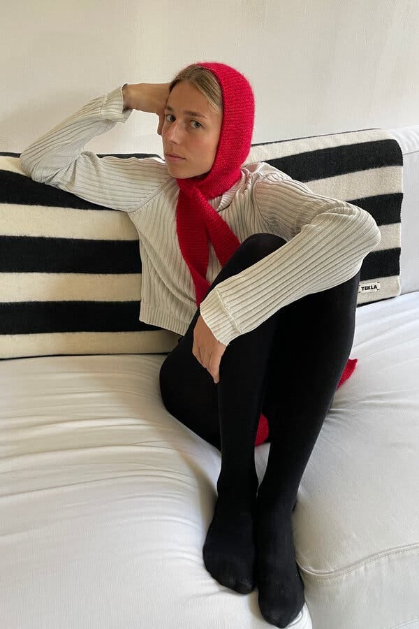 A person with dirty blond hair sitting on a sofa and wearing a red knit bonnet.