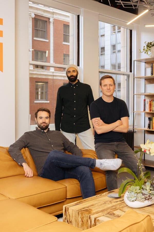 Three men pose for a photograph in front of a large office window.