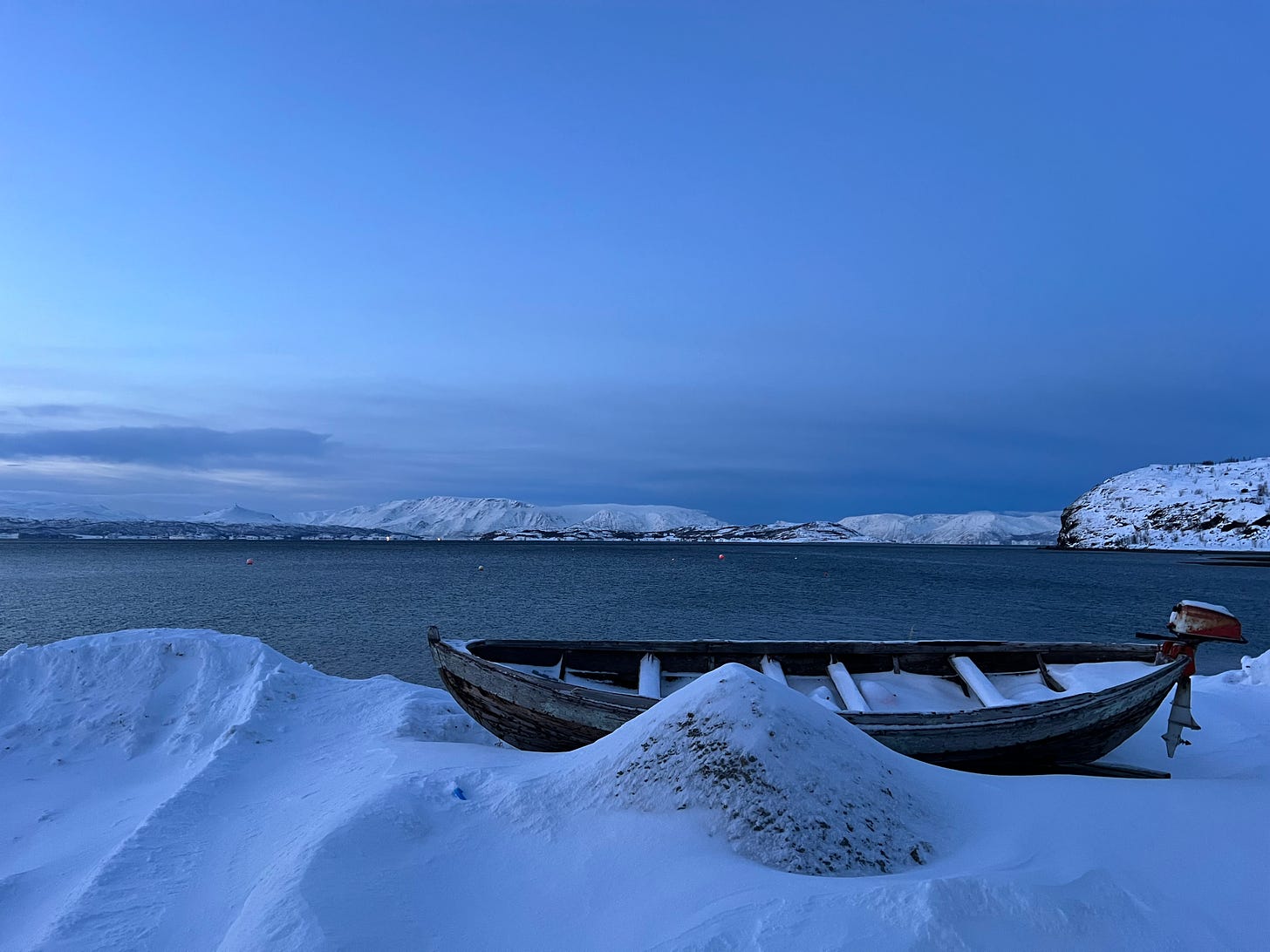 Photo of a snowy fjord with a boat at the front, from Alta in Norway.