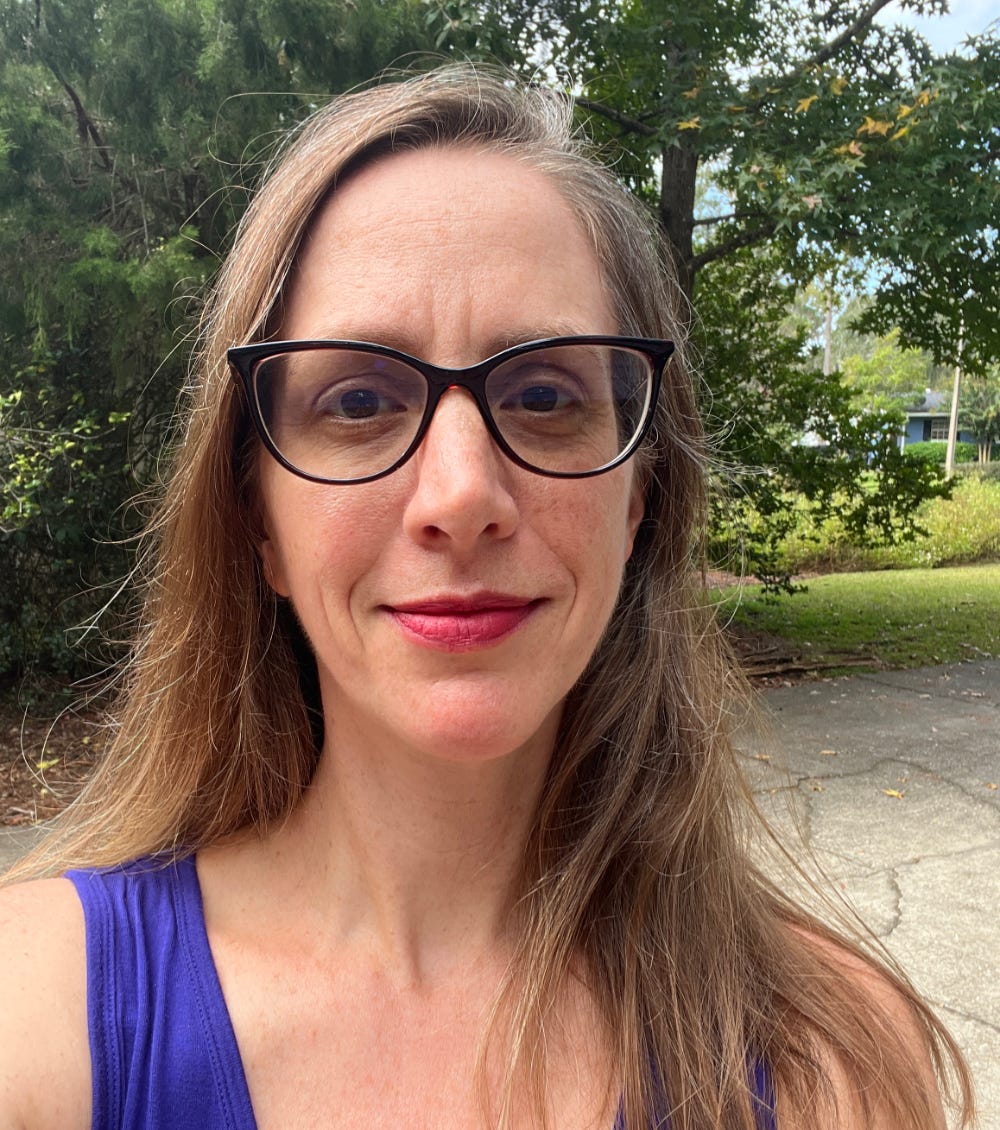 Photo of Sarah Zachrich Jeng, a white woman wearing glasses standing in front of greenery