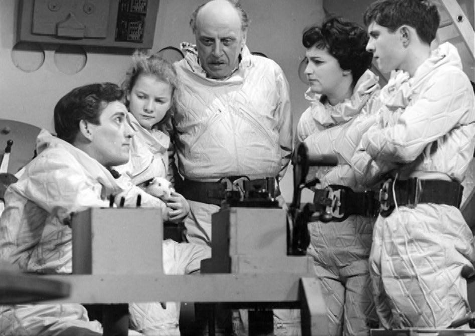 A group shot of five characters in spacesuits but lacking helmets and breathing apparatus, within a space rocket. From left to right is a 30-something man (Conway Henderson), a young girl (Margaret Henderson), a late-middled-aged man (Harcourt Brown), a 30-something woman (Professor Meadows) and a teenage boy (Geoff Wedgwood). They are all light skinned and look intent. The young girl holds a guinea pig.