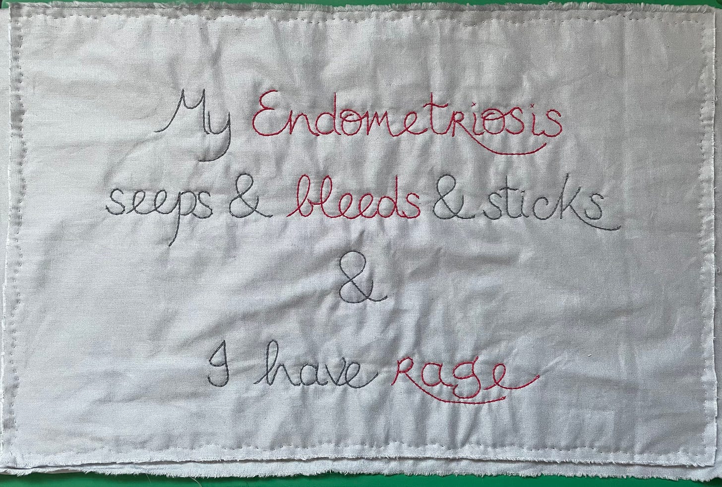 A stitched panel that reads “My Endometriosis seeps and bleeds and I have rage”
