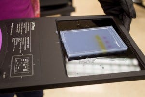 A gel slab on the reading tray, note that you can visually see the migration of the orange dye with the DNA sample. 