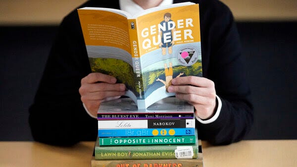 A photo depicts the book Gender Queer open and being read, atop a pile of other banned books.