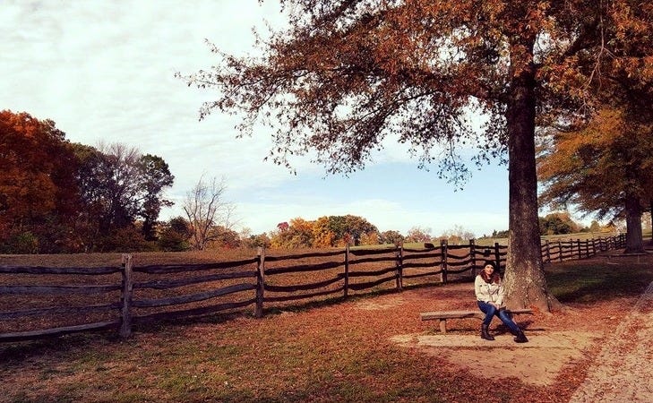 Maria sits on wooden bench against a brown and orange hued backdrop of fall in Mount Vernon