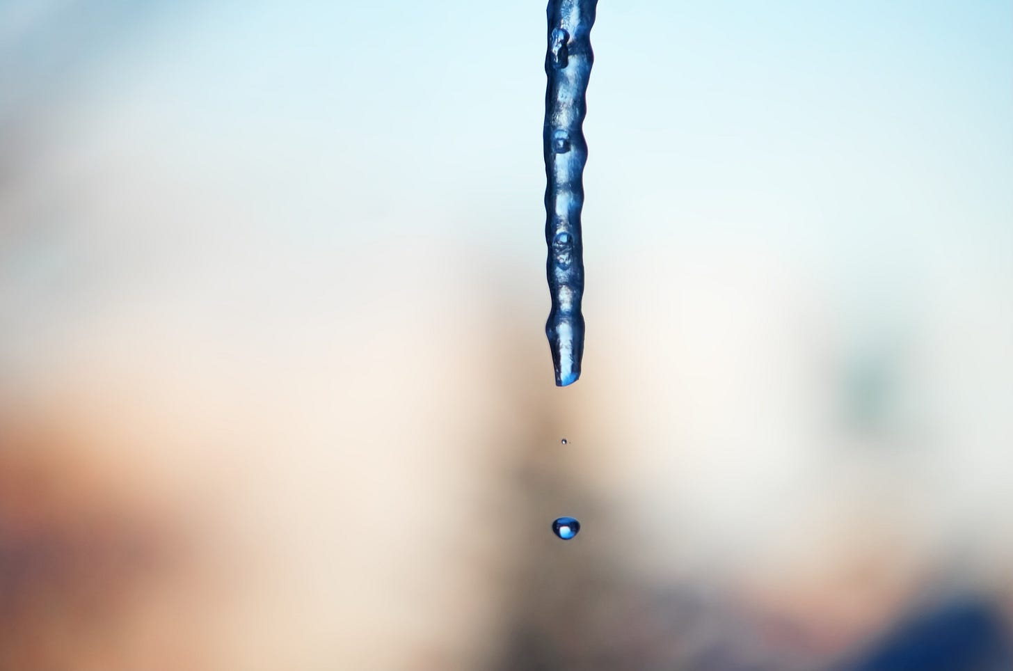 Droplets fall from an icicle against a blue and orange sunset background.