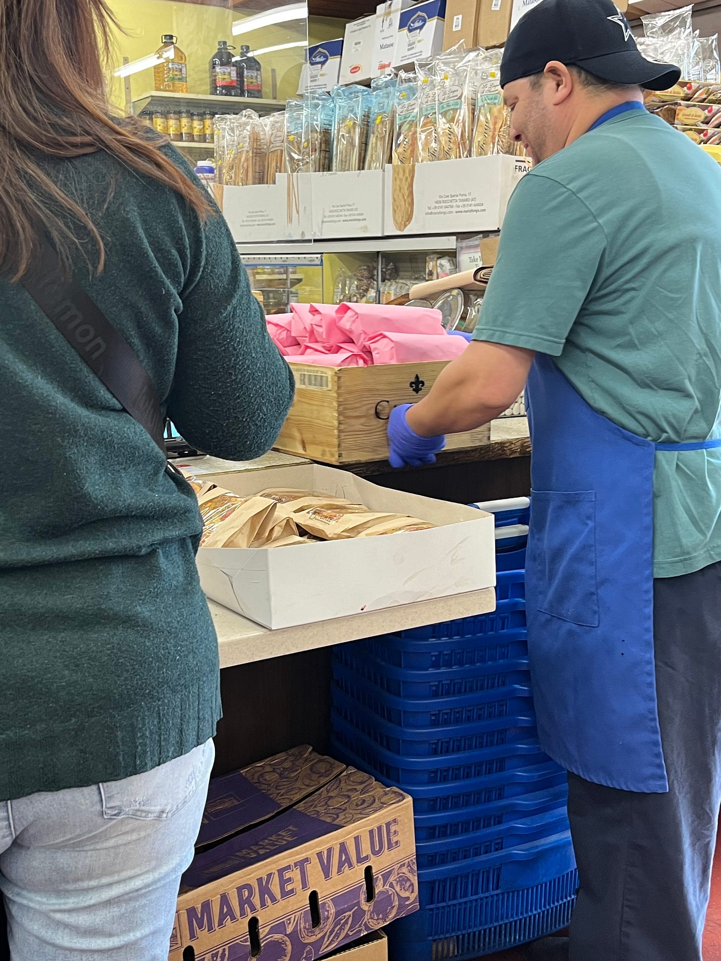 Man restocking pink butcher paper-wrapped sandwiches inside a deli.