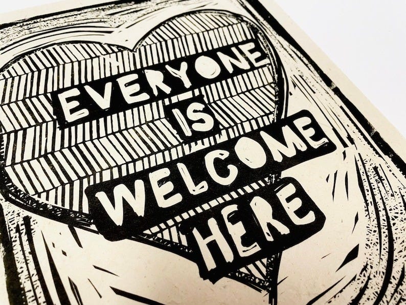 May include: A black and white linocut print of a heart with the words 'Everyone is welcome here' printed on it. May include: A black and white linocut print of a heart with the words 'Everyone is welcome here' printed on it.