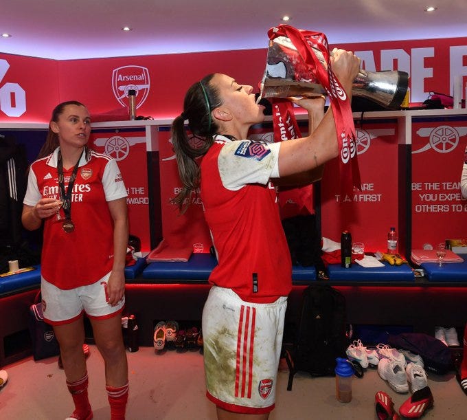 Katie McCabe celebrates with a glass of champagne from the trophy