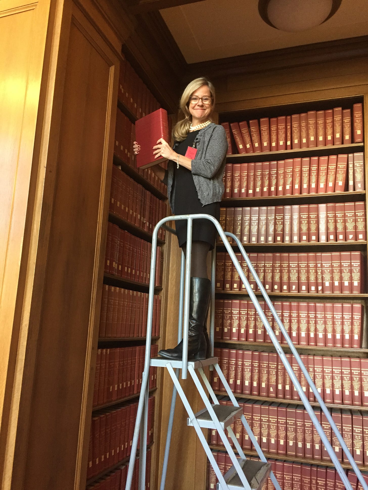 Woman stands on a ladder surrounded by books