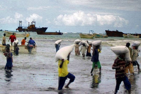 WFP logistics team carrying bags of food through the flooded grounds of Somalia