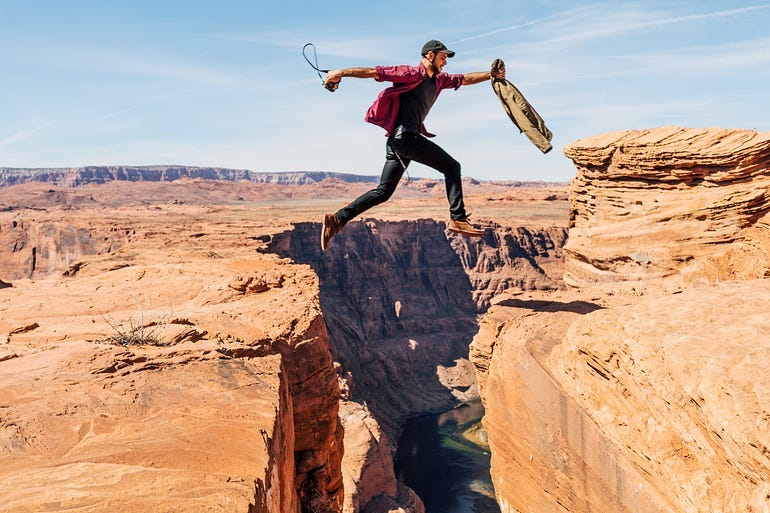 A man jumping over a gap in mid-air. There’s a distinct valley in between two cliffs.