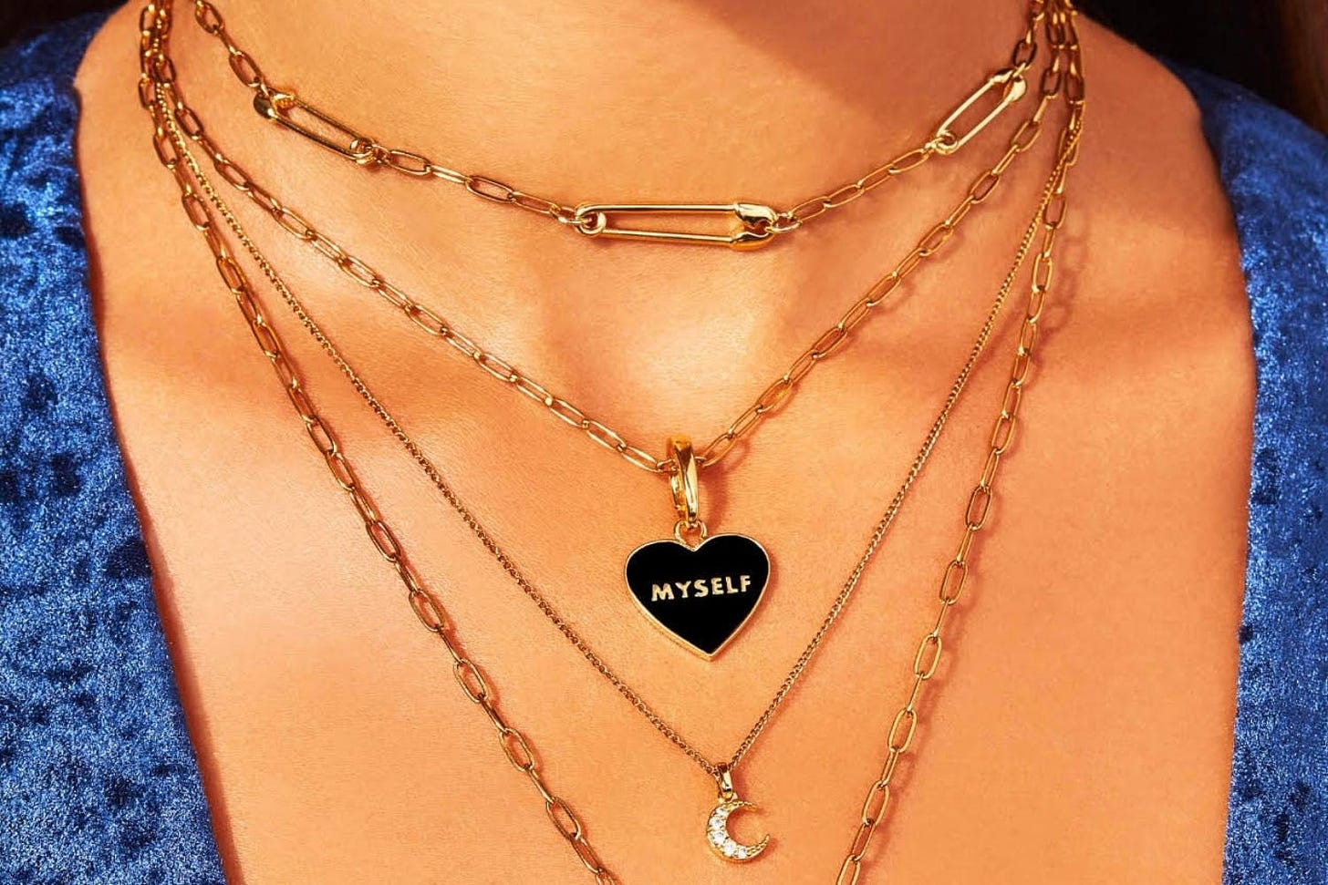 Woman's neck with four gold necklaces, one is a heart that reads "myself"