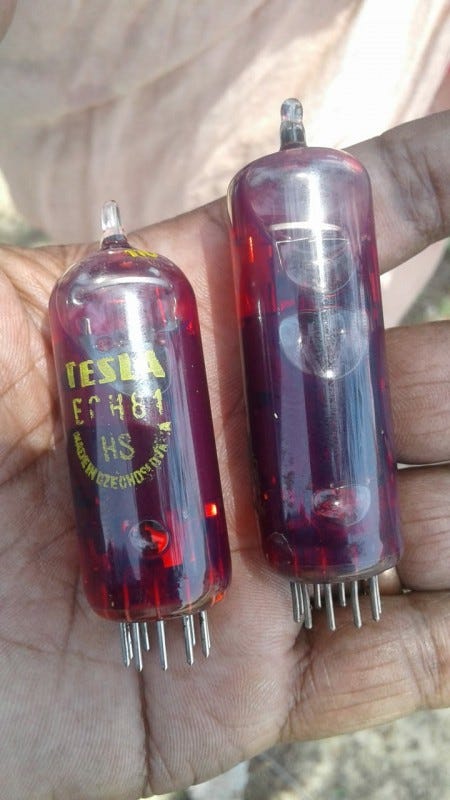 Someone holding two small glass tubules in their hand. The tubes contain red fluid, and have metal prongs sticking out the bottom. One has yellow text printed on it, fading, that says "TESLA" and what appears to be "MADE IN CZECHOSLOVAKIA"