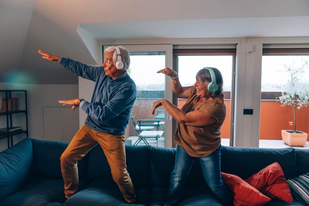 Carefree elders dancing on the couch while listening to music.