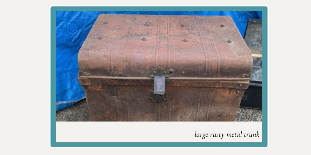 a large rusty metal trunk with a loose lock on a blue tarp background