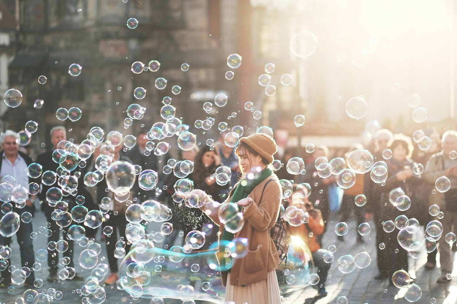 Woman in winter clothing plays with floating bubbles while a crowd watches