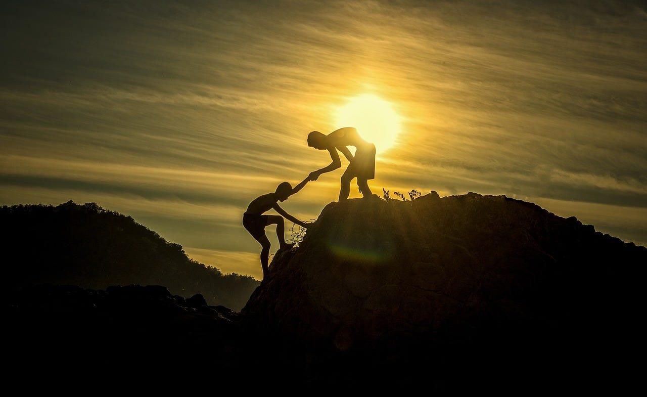 Man helping another man up to the top of a mountain