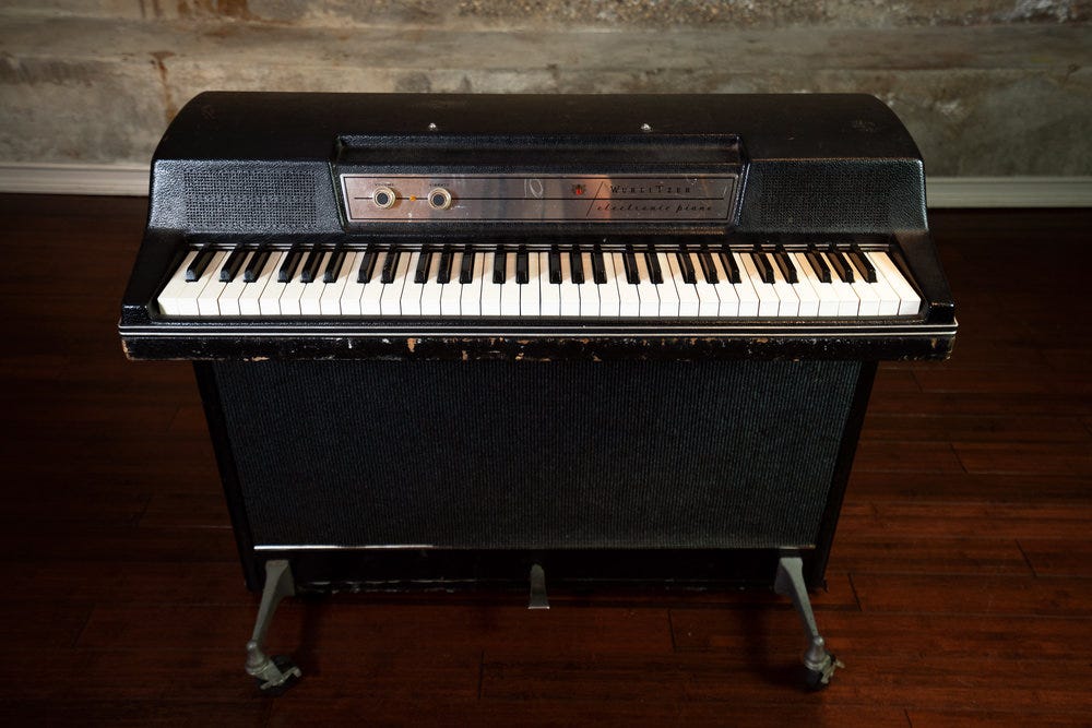 A photo of a Wurlitzer 203w with white keys and a lot of chips along the wooden base.