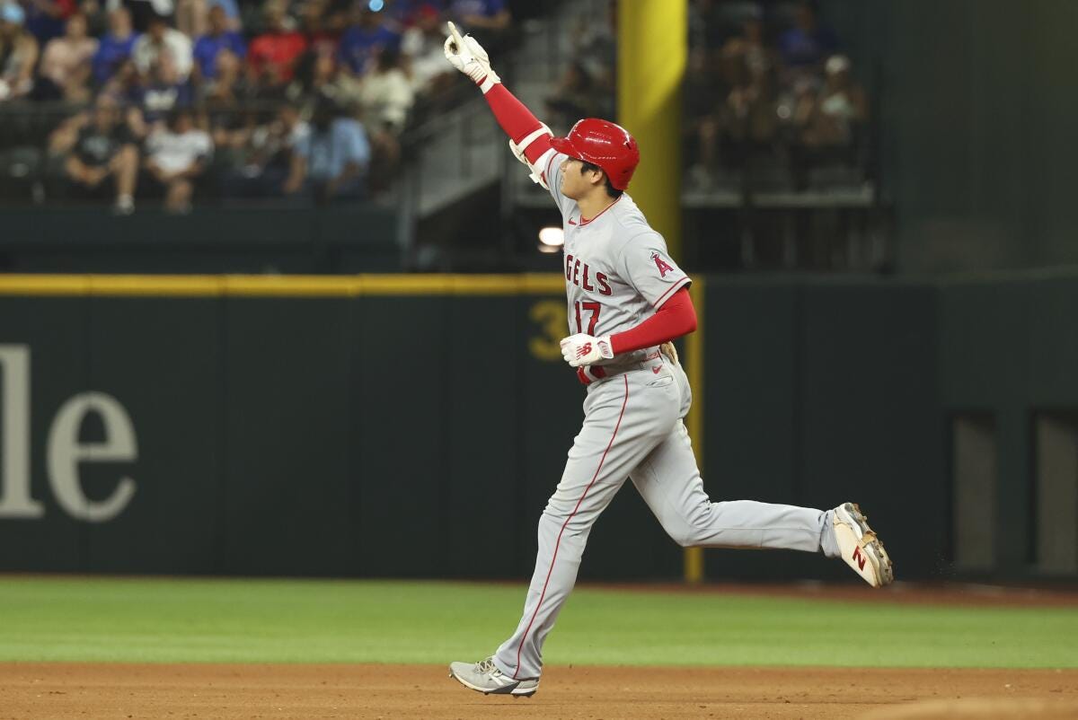 Ohtani, wearing a red and white Angels uniform, salutes the crowd as he runs to the next base.