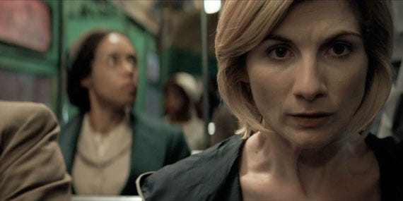 This image shows, in the foreground, the Thirteenth Doctor (played by Jodie Whittaker) sitting on a Montgomery, Alabama bus on 1 December 1955 and looking sick to her stomach as she allows Rosa Parks (played by Vinette Robinson), who sits in the background, to be confronted by bus driver James Blake. The Doctor blocks Blake from view, but Rosa looks up at him from her seat. This image shows, in the foreground, the Thirteenth Doctor (played by Jodie Whittaker) sitting on a Montgomery, Alabama bus on 1 December 1955 and looking sick to her stomach as she allows Rosa Parks (played by Vinette Robinson), who sits in the background, to be confronted by bus driver James Blake. The Doctor blocks Blake from view, but Rosa looks up at him from her seat.