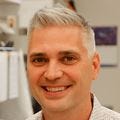 Jonah Sacha, Ph.D., has a white shirt on and gray hair, smiling in his lab.