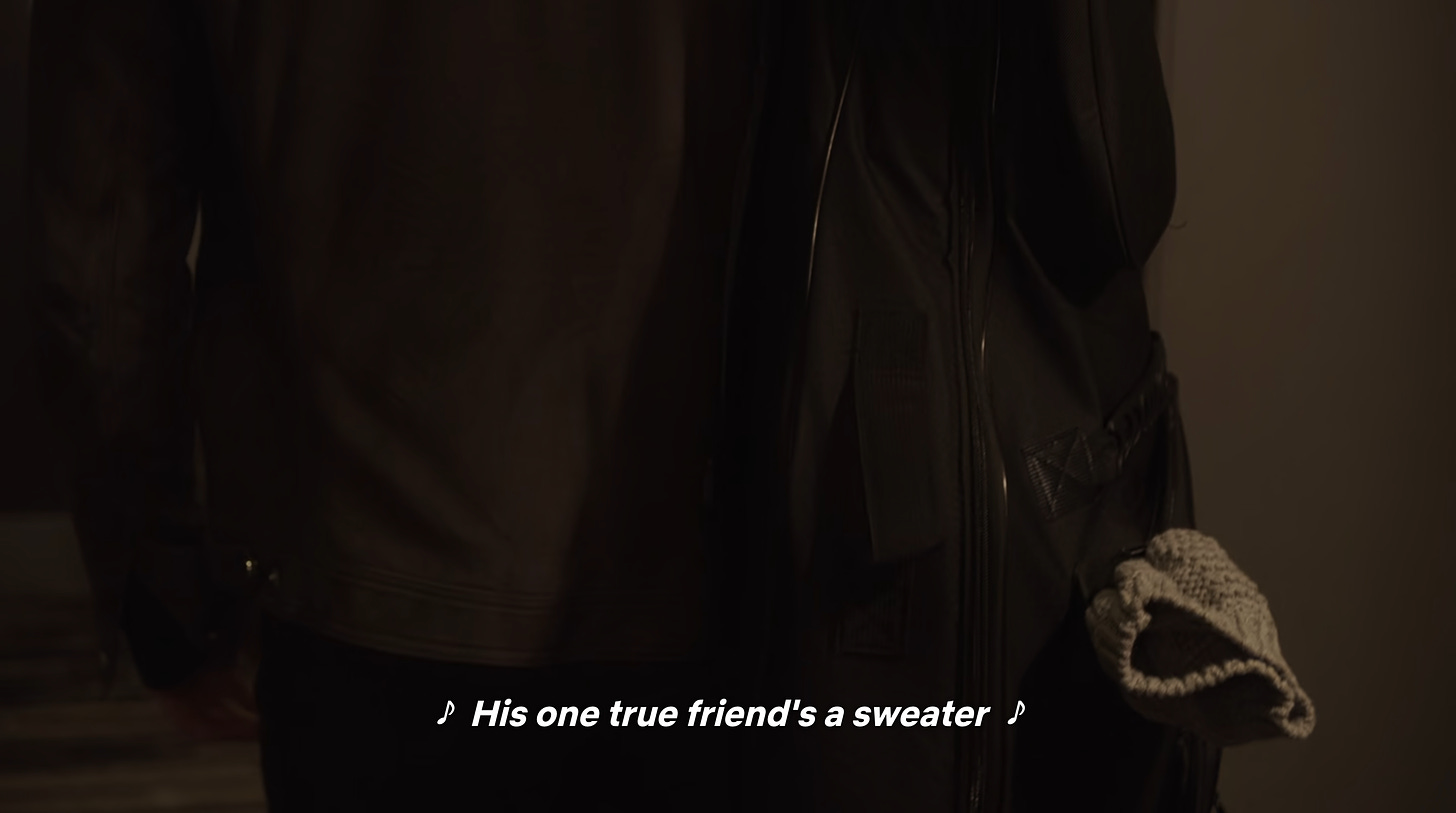 Thomas Doherty as Gray Holland in GIRLS5EVA. It's a closeup of his backpack, which has a white sweater peeking out of it. The captions feature the lyrics, "His one true friend's a sweater"