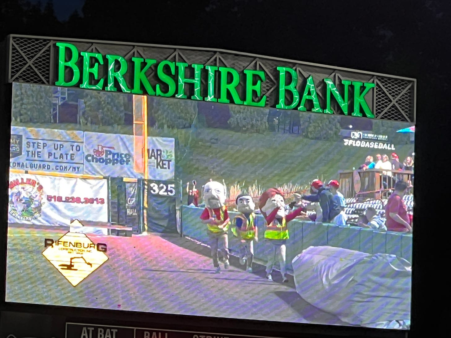 the three mayors racing on the big screen at the ballpark. Rifenbeurg's logo in the bottom left.
