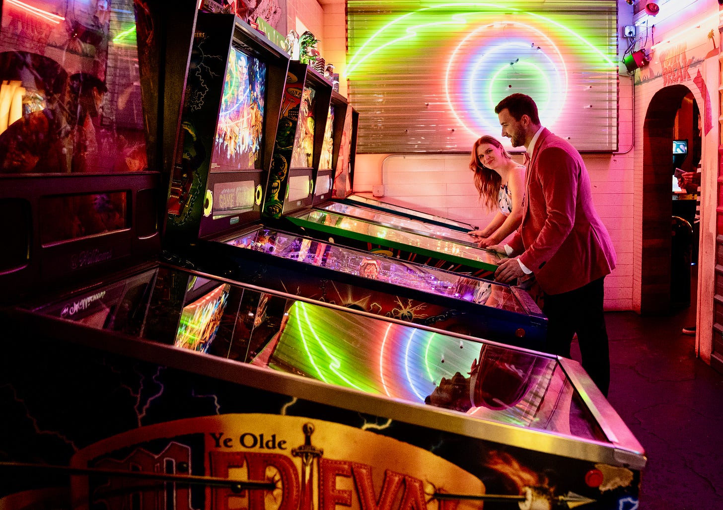 Photo of man and woman playing pinball in dimly lit arcade bar