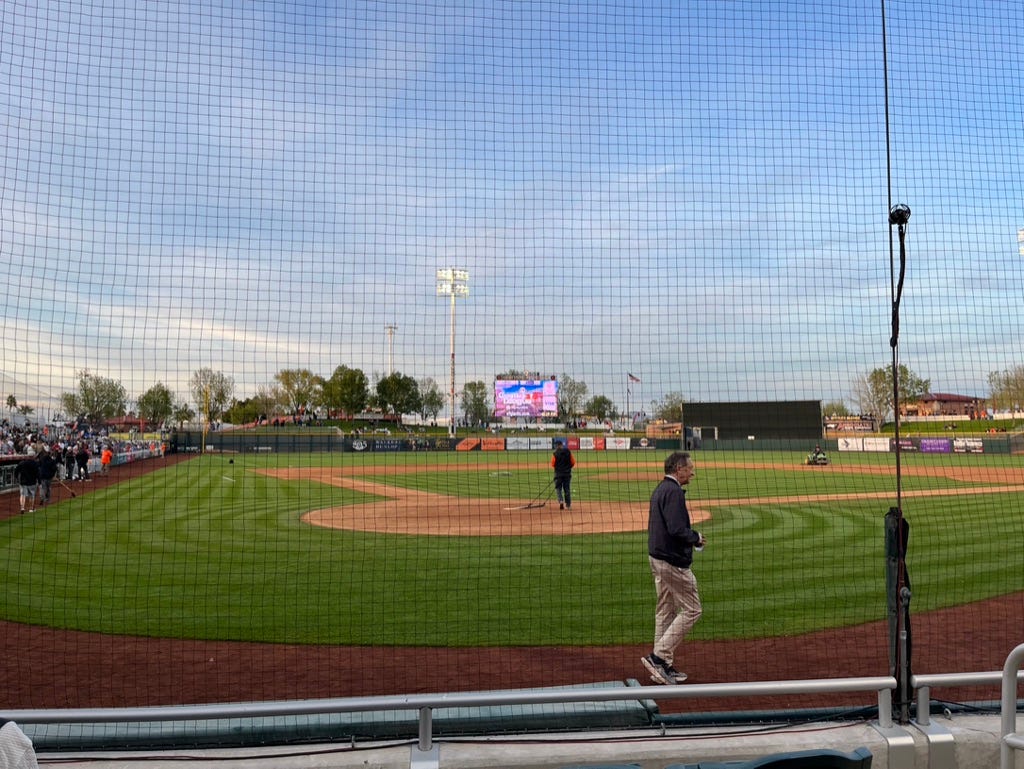 Scottsdale Stadium field being prepared for an evening game with Larry Baer walking behind home plate.